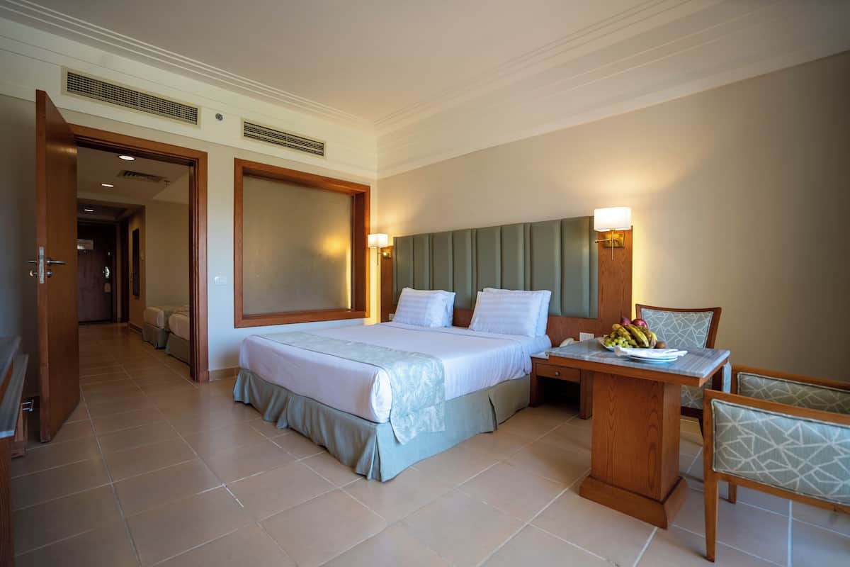 Une chambre d’hôtel dotée d’un grand lit, de tables de chevet, d’un petit bureau avec une chaise et d’un coin repas comprenant une table et des chaises.
