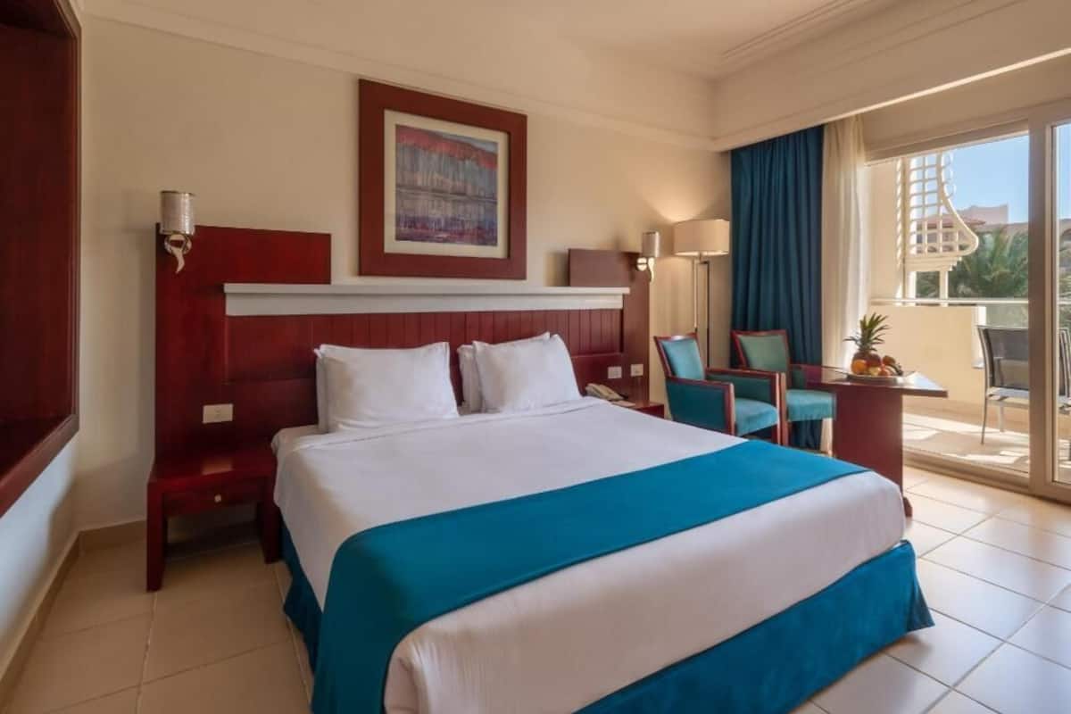 Une chambre d’hôtel avec un grand lit, un bureau, une chaise, une lampe et une vue sur l’extérieur.