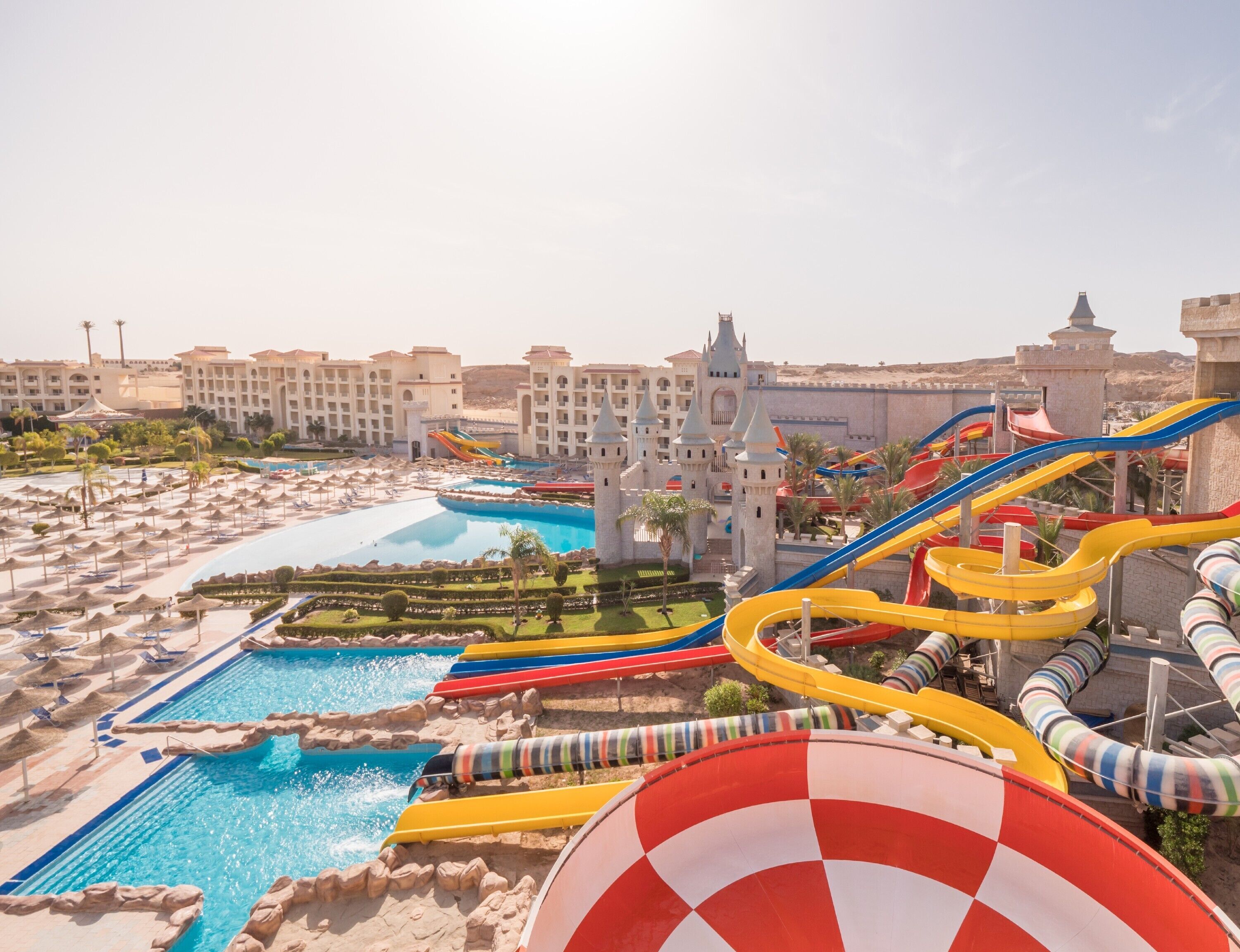 Ein Resort mit einem großen Pool, mehreren Wasserrutschen und einem schlossartigen Gebäude im Hintergrund.