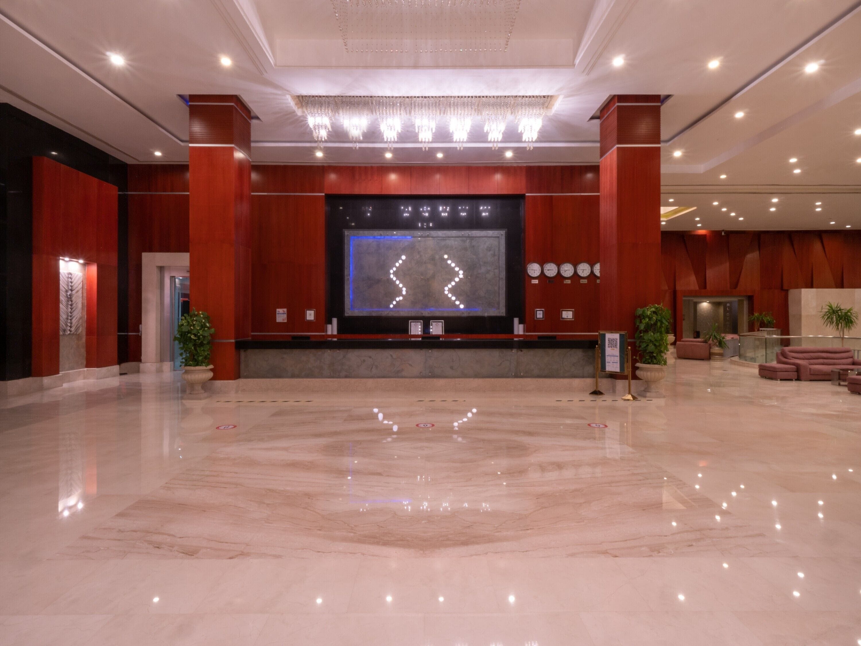 A spacious lobby with a large digital display, marble flooring, and red wooden paneling.