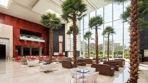 Eine geräumige Lobby mit hohen Decken, großen Fenstern und verschiedenen Sitzgelegenheiten, darunter Sofas und Sessel.