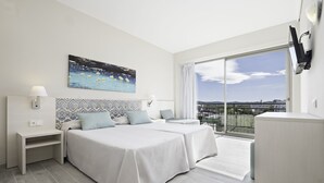 A hotel room with two beds, a large window with a city view, a painting on the wall, and a flat-screen TV mounted on the wall. - azuLine Hotel Llevant (Sant Antoni de Portmany)