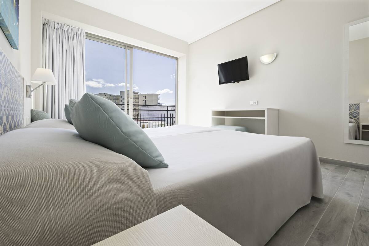 A modern hotel room with a large bed, a TV mounted on the wall, and a balcony with a view of the city.