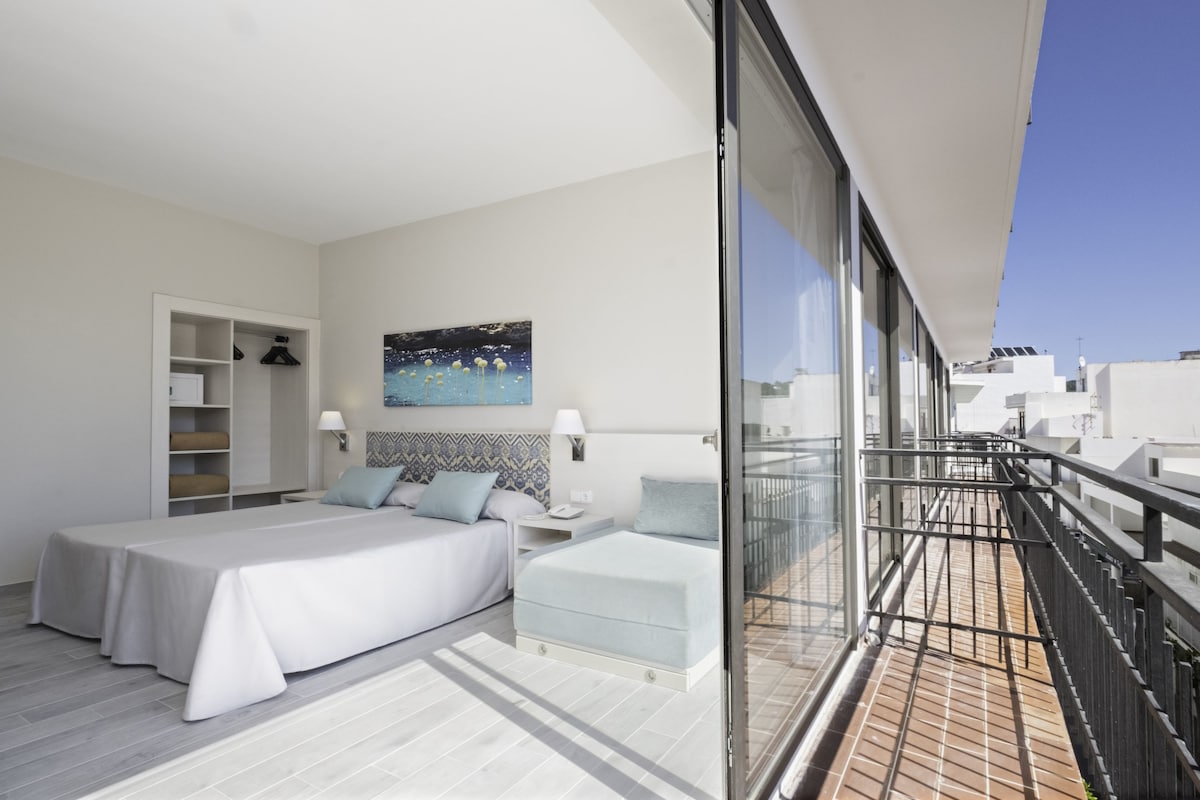 A modern hotel room with a large bed, a desk, and a balcony with a railing.