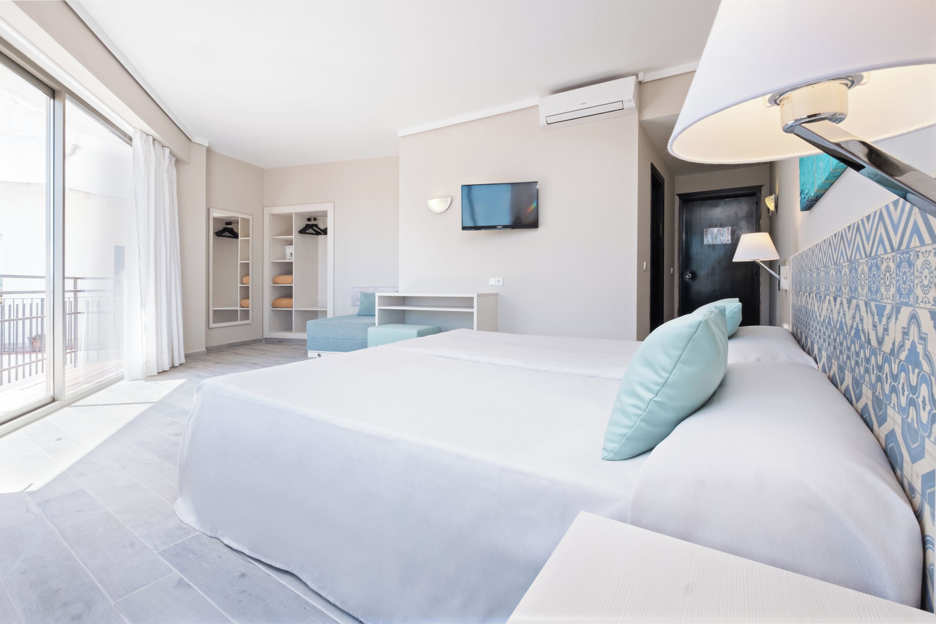 A modern hotel room with a large bed, a desk, a TV, and a balcony.
