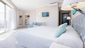 A modern hotel room with a large bed, a desk, a TV, and a balcony.