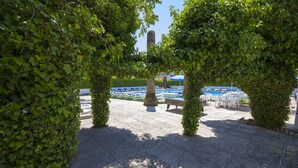 A paved outdoor area with a pool, lounge chairs, and a tall stone structure. - azuLine Hotel Llevant (Sant Antoni de Portmany)