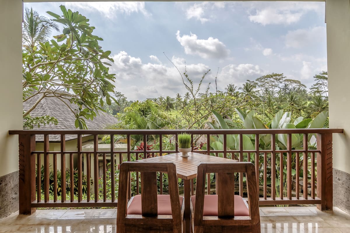 A wooden table and chairs on a balcony with a view of lush greenery and a tiled floor.
