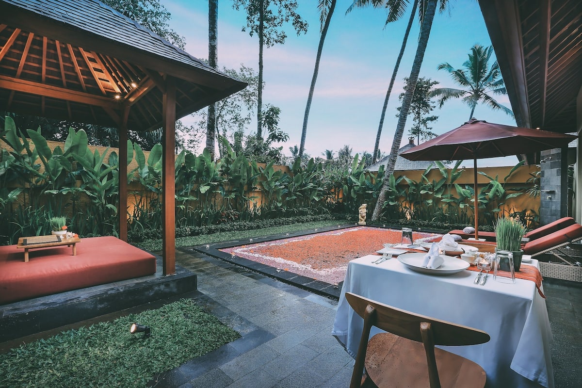 An outdoor dining area with a table set for two, surrounded by lush greenery and palm trees.