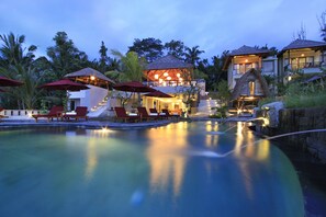 A resort with a swimming pool, lounge chairs, and thatched-roof structures.