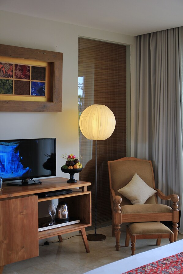 Habitación de hotel con escritorio de madera, televisor, lámpara de pie, silla y ventana con cortinas.