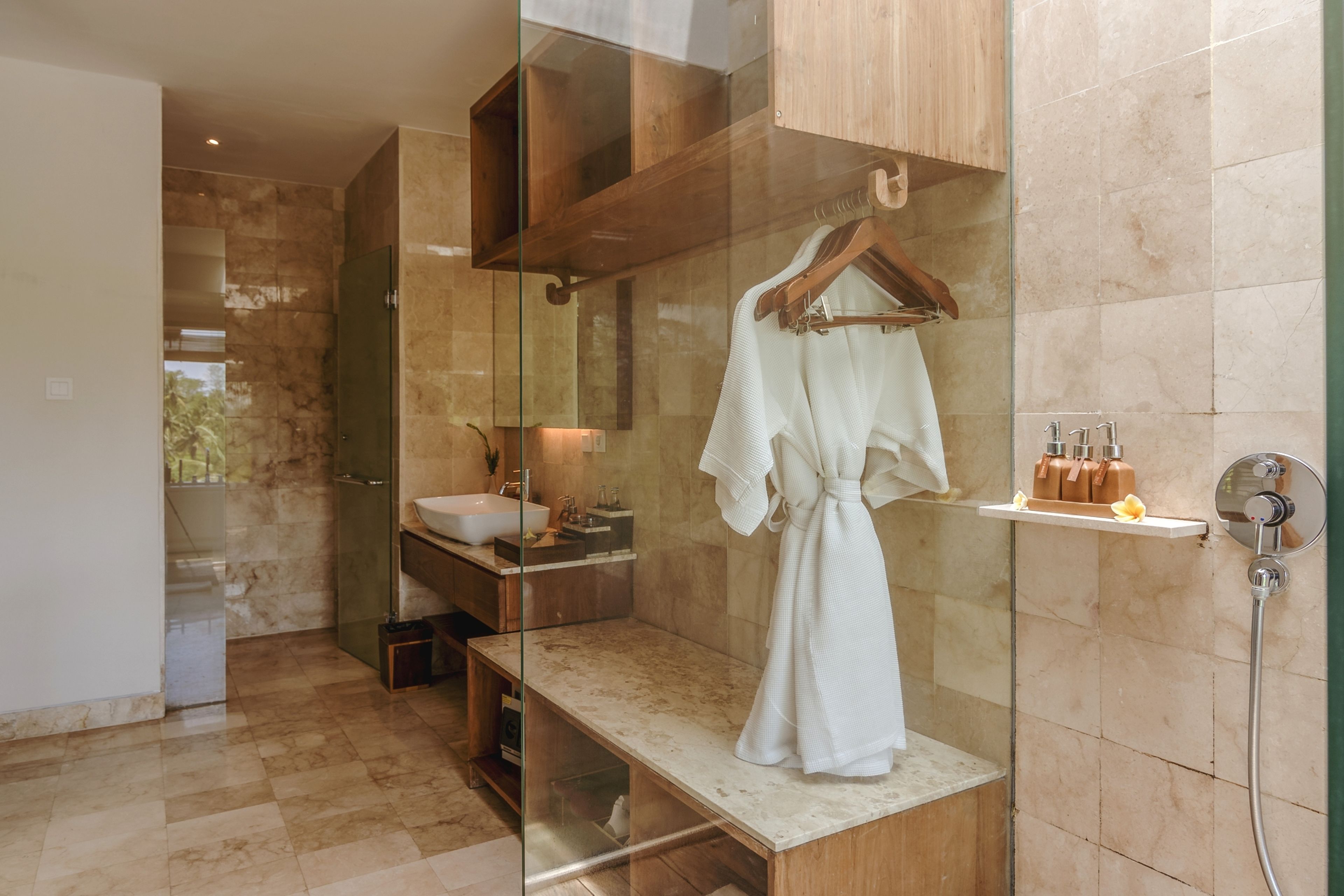 A modern bathroom with a glass-enclosed shower, a wooden vanity, and a robe hanging on a rack.