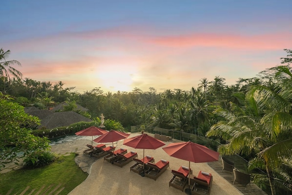 A resort with a pool, red umbrellas, and lounge chairs.
