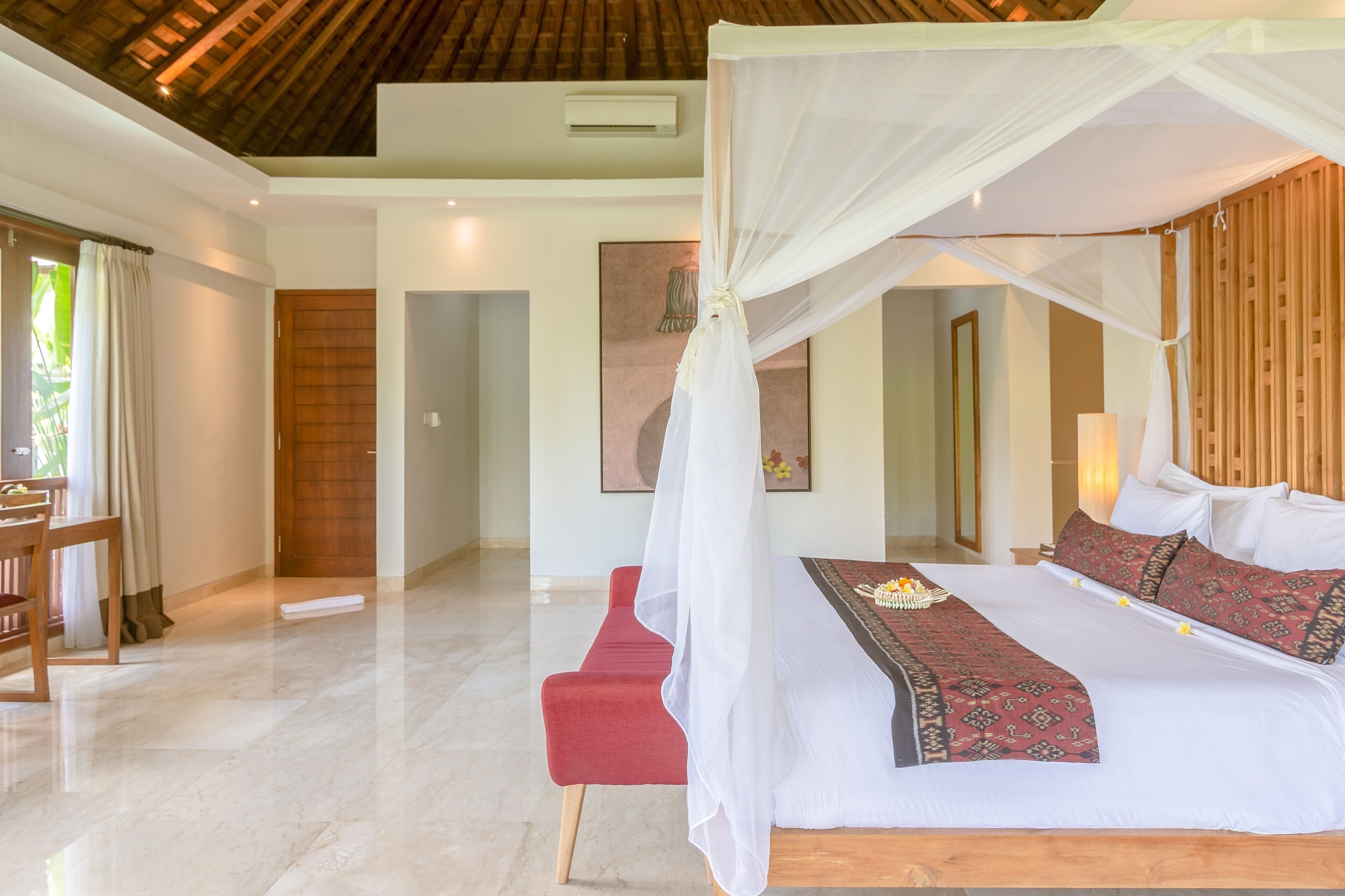 Un dormitorio con cama con dosel, un banco rojo y un área de comedor con mesa y sillas.