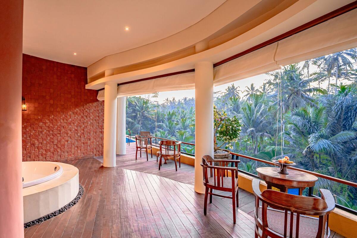 A spacious balcony with wooden flooring, a hot tub, and several wooden chairs.