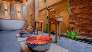 A spa area with a large bathtub, two bowls with red contents, wooden stools, and a brick wall. - Puri Sebali Resort (Ubud)