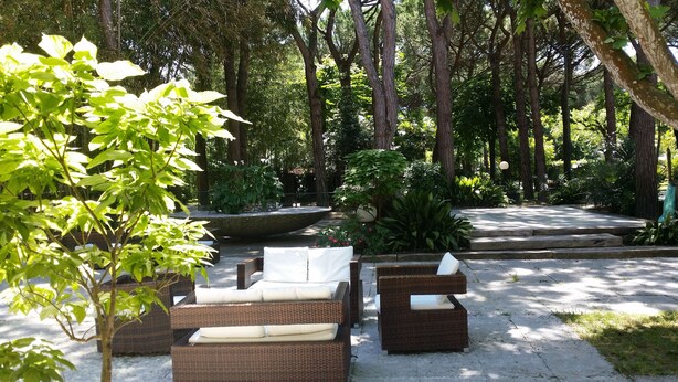 Une terrasse de jardin aménagée avec des meubles en osier, une fontaine en pierre et une végétation luxuriante.