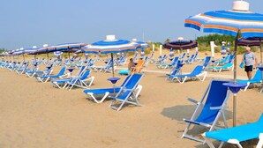 Une plage bordée de rangées de chaises longues bleues et de parasols à rayures.