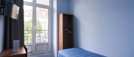 Un dormitorio con una cama individual, un armario de madera, un escritorio con silla, un televisor y una ventana con cortinas.