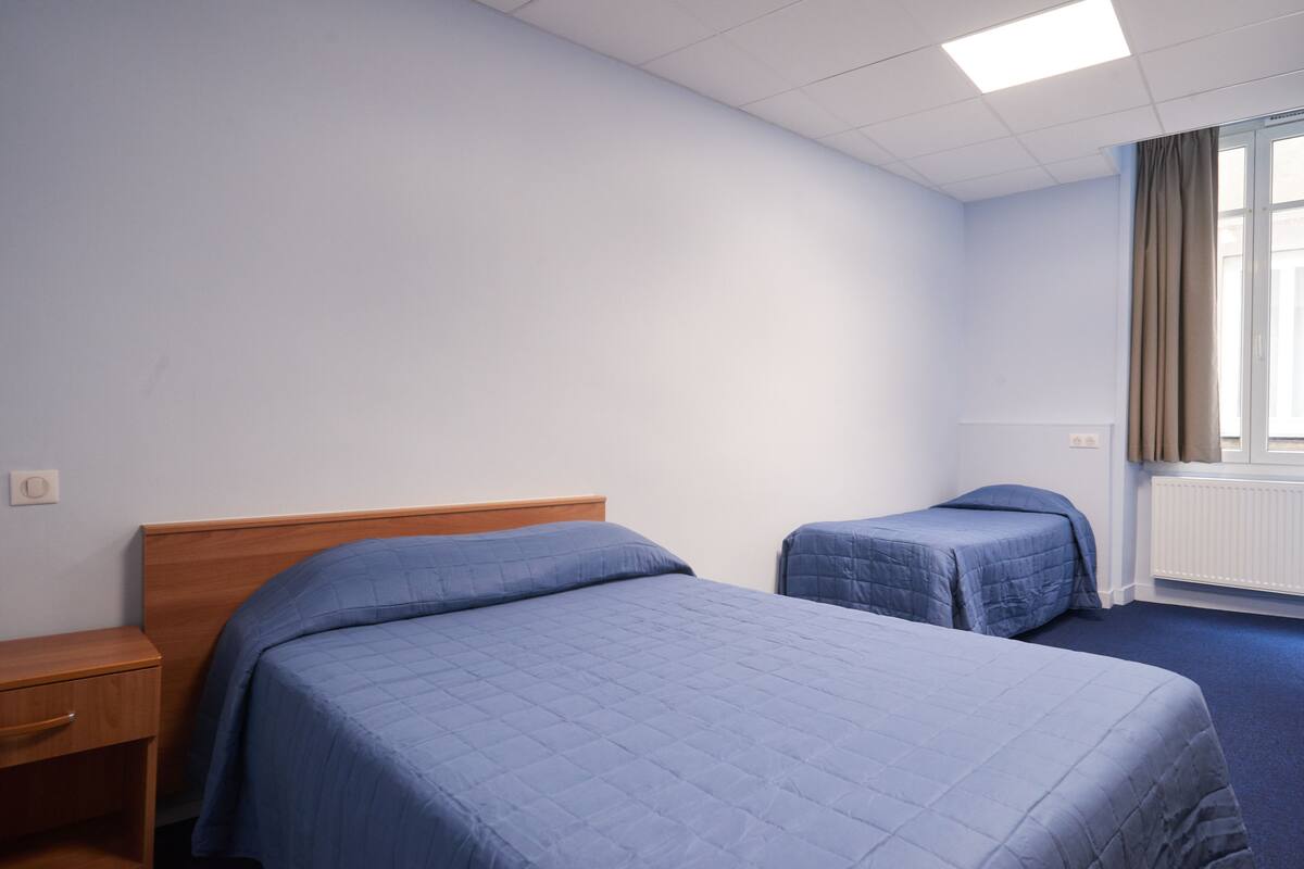 Une chambre d’hôtel avec deux lits, une table de chevet en bois et une fenêtre avec des rideaux.