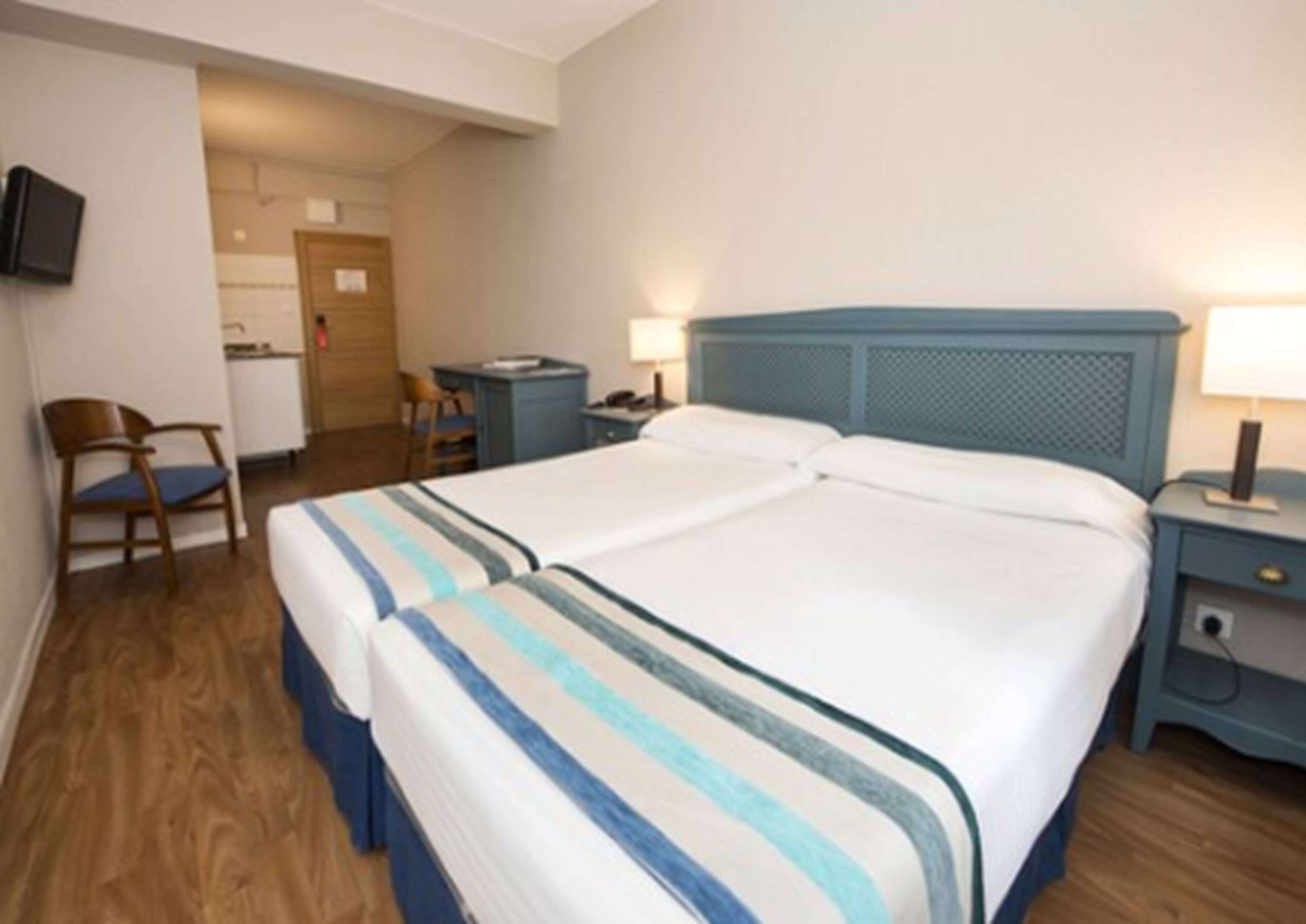 Un lit double avec une parure de lit  à rayures, un bureau avec une chaise, un téléviseur fixé au mur et une porte donnant sur une salle de bain.