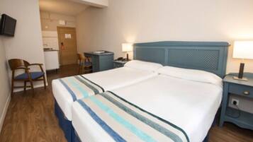 A double bed with striped bedding, a desk with a chair, a television on the wall, and a door leading to a bathroom.