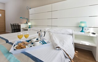 Habitación de hotel con cama, mesita de noche y escritorio con silla. Hay una bandeja con alimentos y bebidas sobre la cama.
