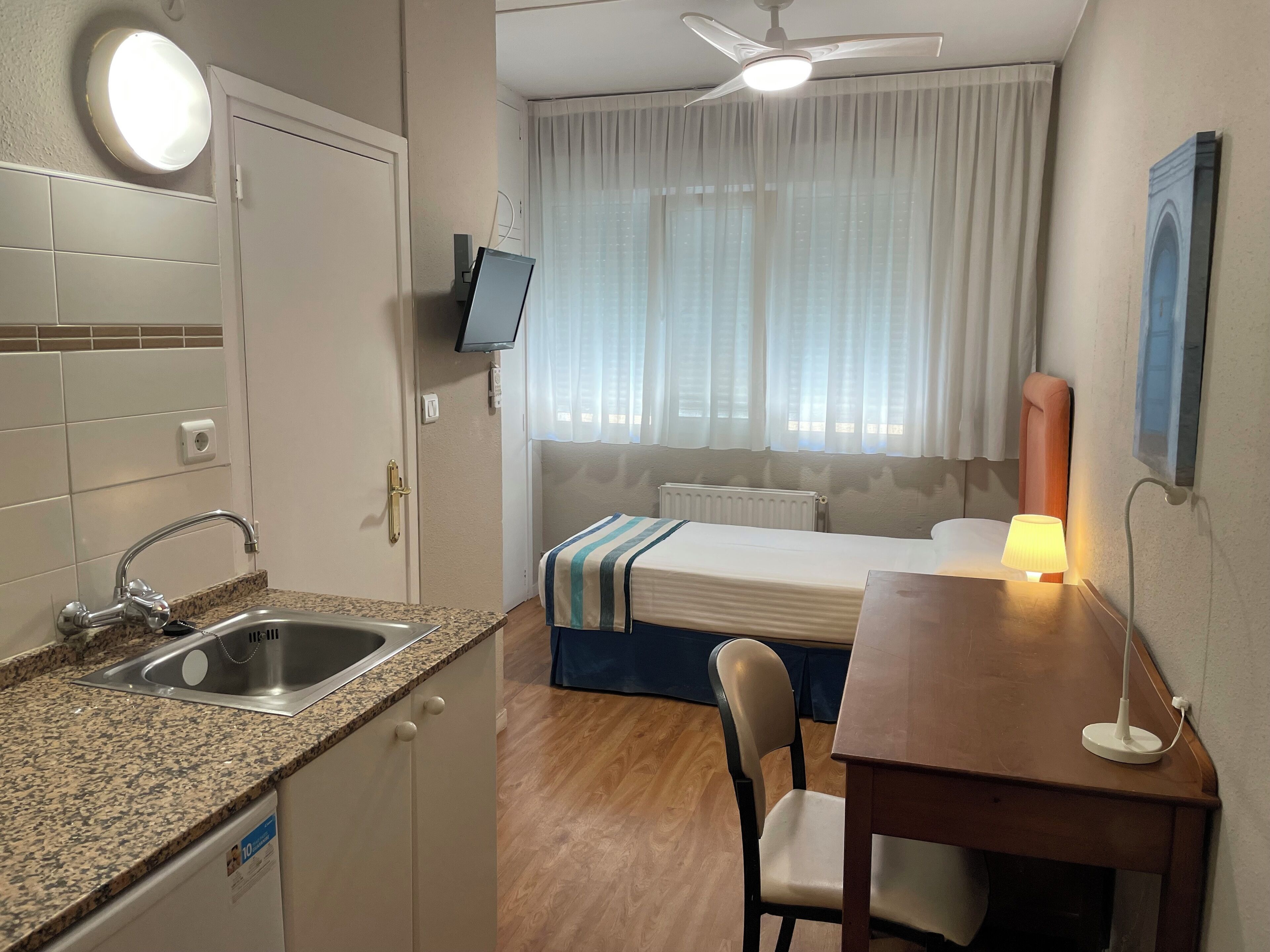 A compact hotel room with a kitchenette, a bed, a desk, and a chair.