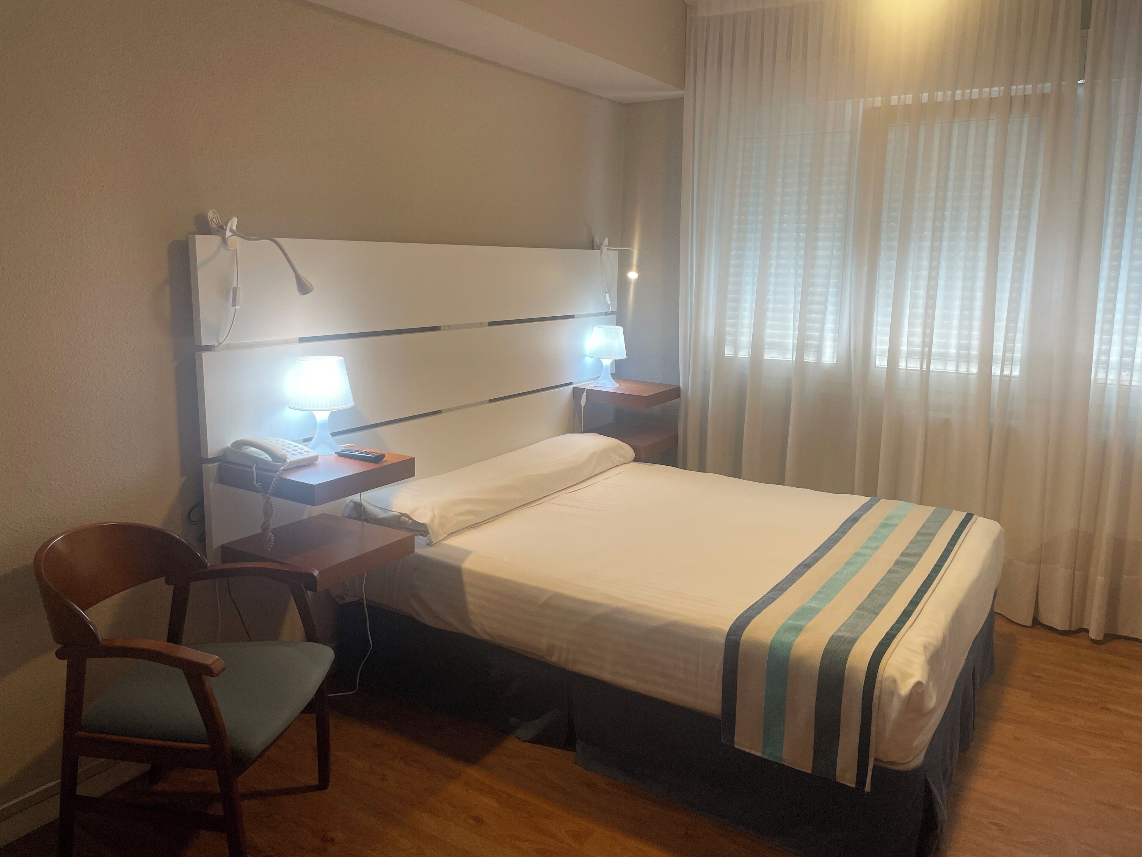 Quarto de hotel com uma cama, uma escrivaninha com luminária, uma cadeira e um telefone.