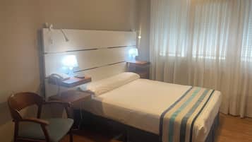 Quarto de hotel com uma cama, uma escrivaninha com luminária, uma cadeira e um telefone.