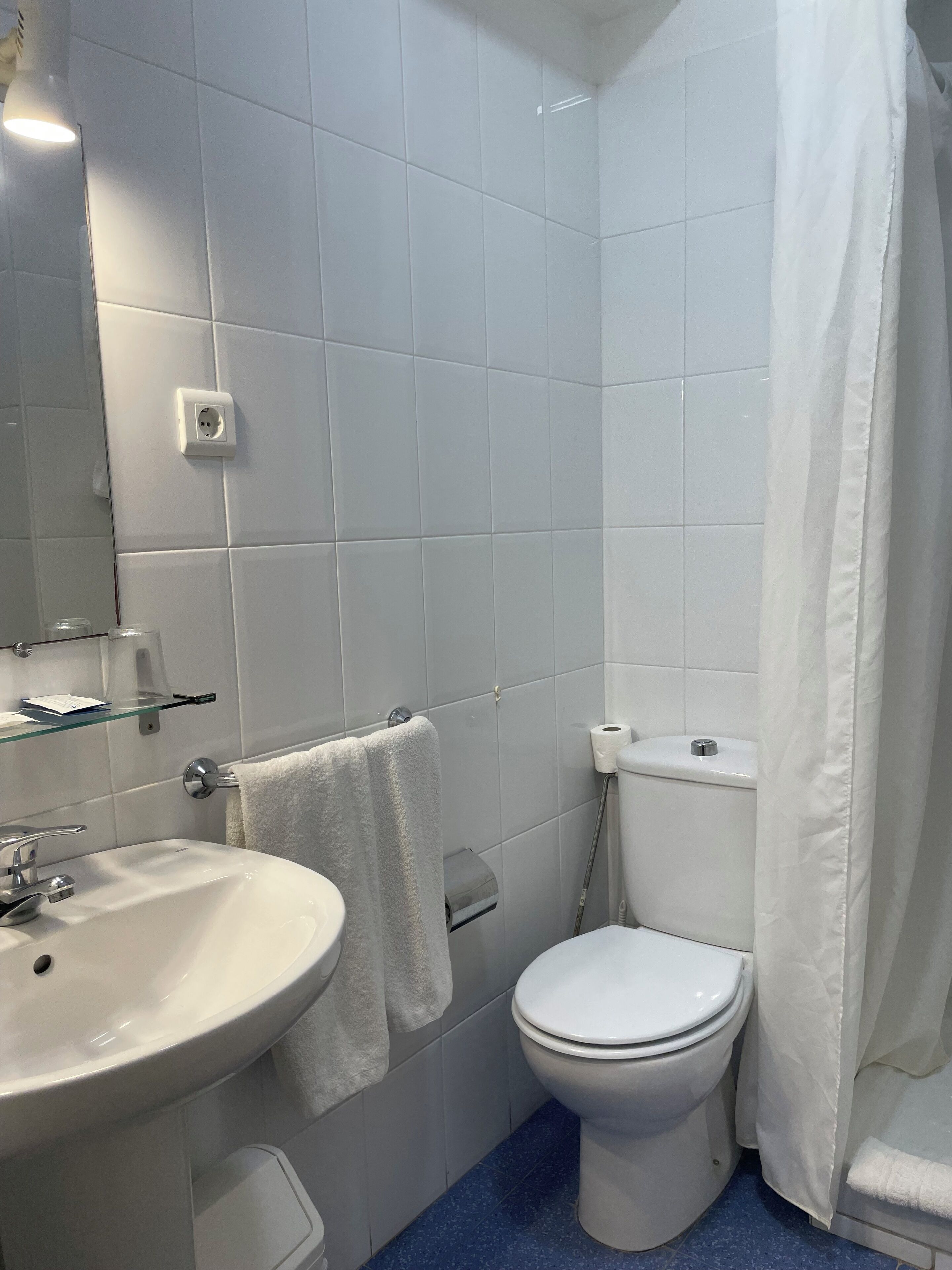 A bathroom with a white sink, mirror, and toilet, and a shower curtain.