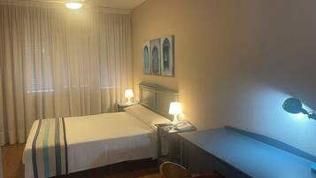A hotel room with a bed, a desk, a chair, a lamp, and a ceiling fan.