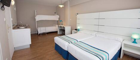 Habitación de hotel con literas, un escritorio con silla, un lavamanos pequeño y un televisor montado en la pared.