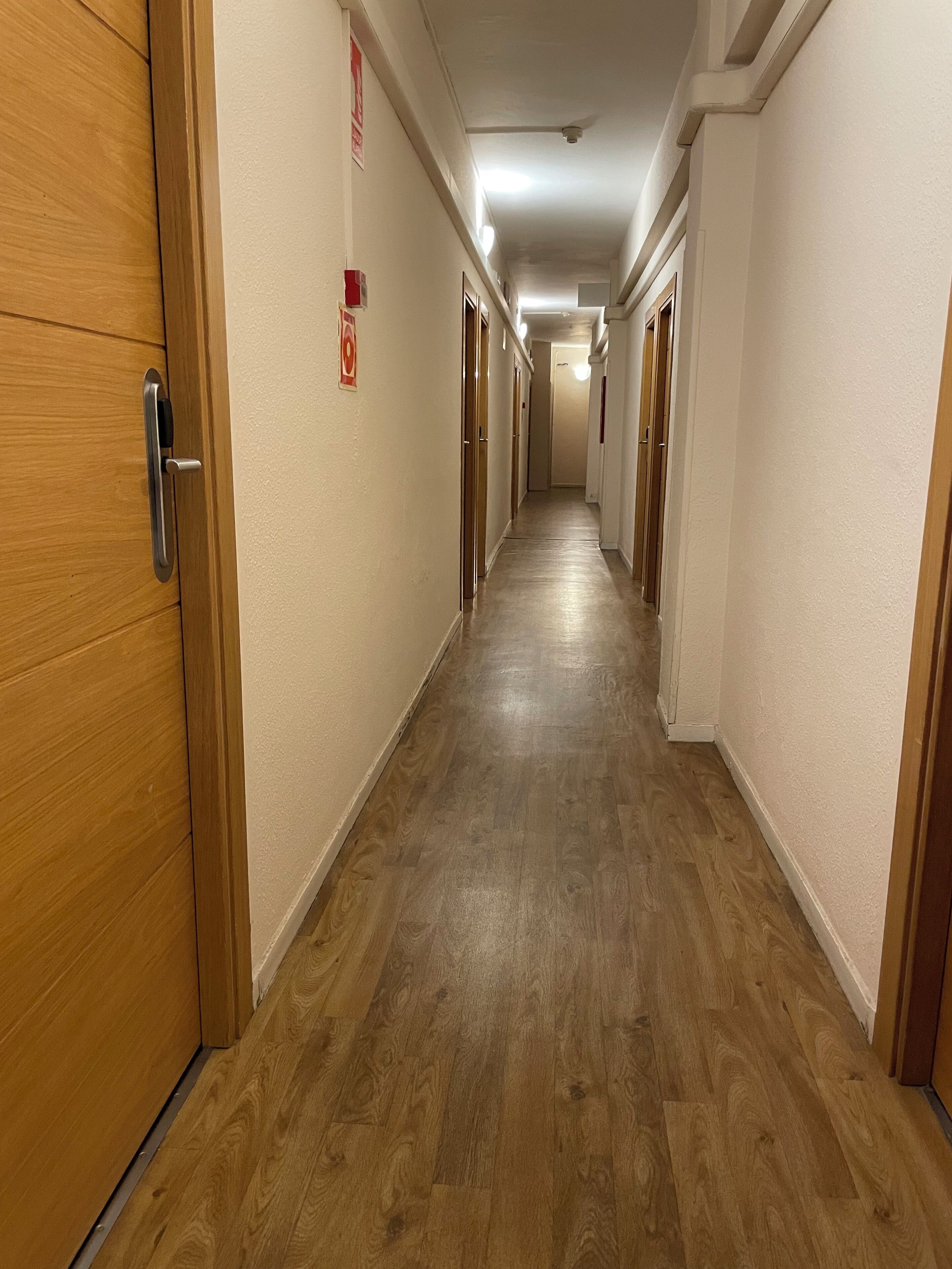 Un pasillo largo y estrecho con puertas de madera a ambos lados, que conduce a habitaciones individuales.
