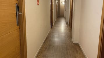Un pasillo largo y estrecho con puertas de madera a ambos lados, que conduce a habitaciones individuales.