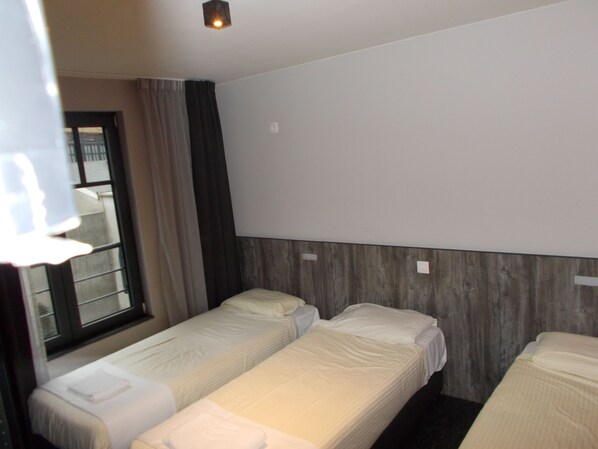 Una habitación de hotel con dos camas individuales, una ventana con cortinas y un cabecero de madera.