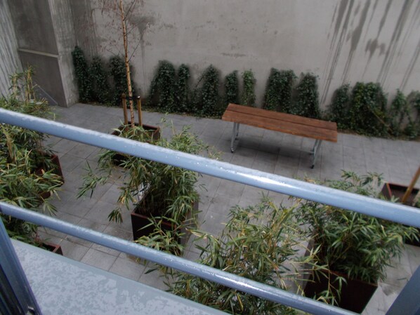 Un patio con un banco de madera, plantas en macetas y una barandilla de metal.