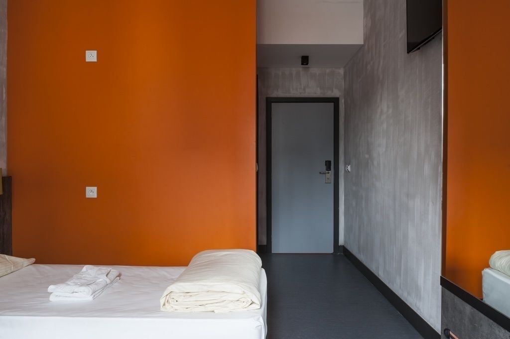 A hotel room with two beds, a grey door, and a TV mounted on the wall.