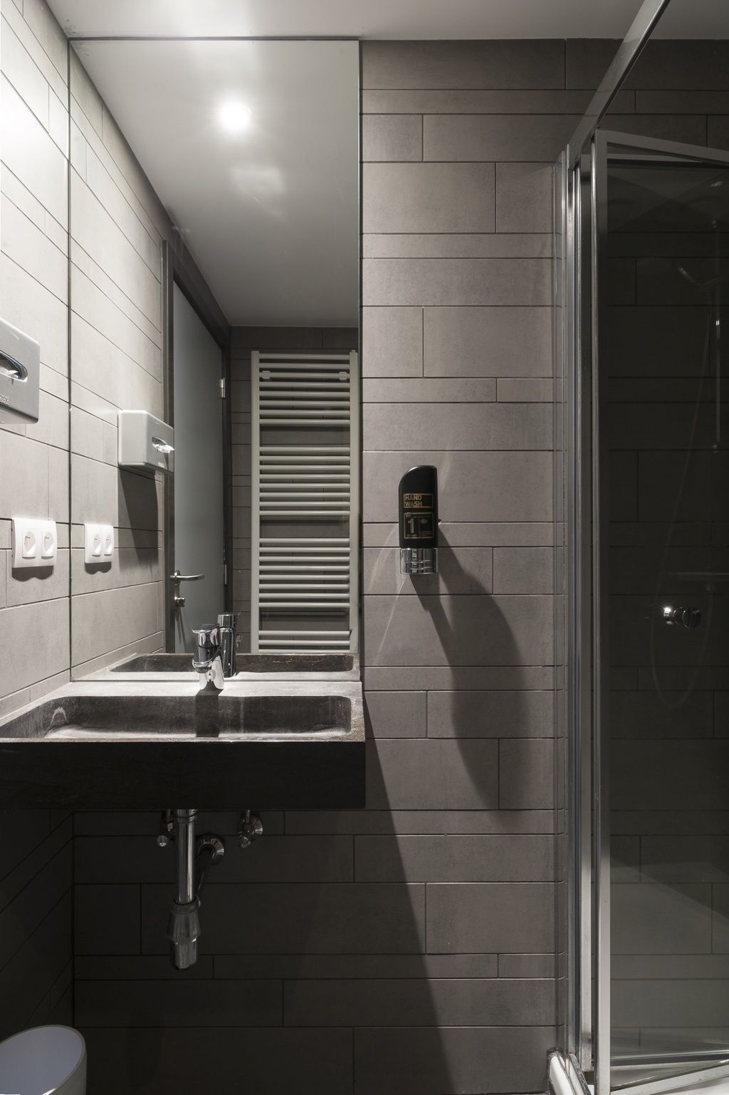 Une salle de bain moderne équipée d’un lavabo, d’un sèche-mains et d’une douche à parois de verre.
