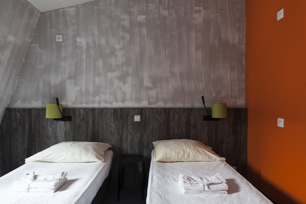 A room with two beds, each with white linens and pillows, and a small table between them.