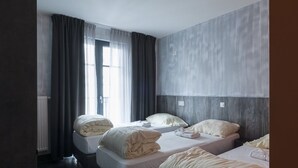 A hotel room with three beds, a large window with curtains, and a modern design. - BRXXXL5 - Hostel (Brussels)