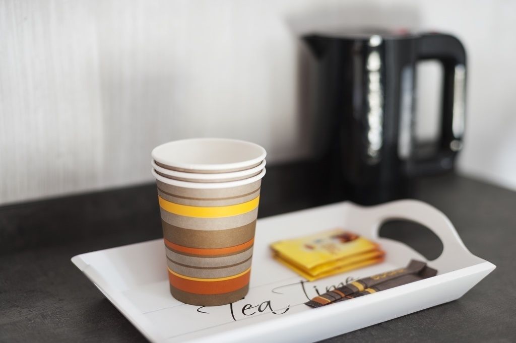 A stack of striped cups on a tray with a tea box and a kettle in the background.