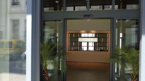 A hotel entrance with a reception desk, two potted palm plants, and a glass door. - BRXXXL5 - Hostel (Brussels)