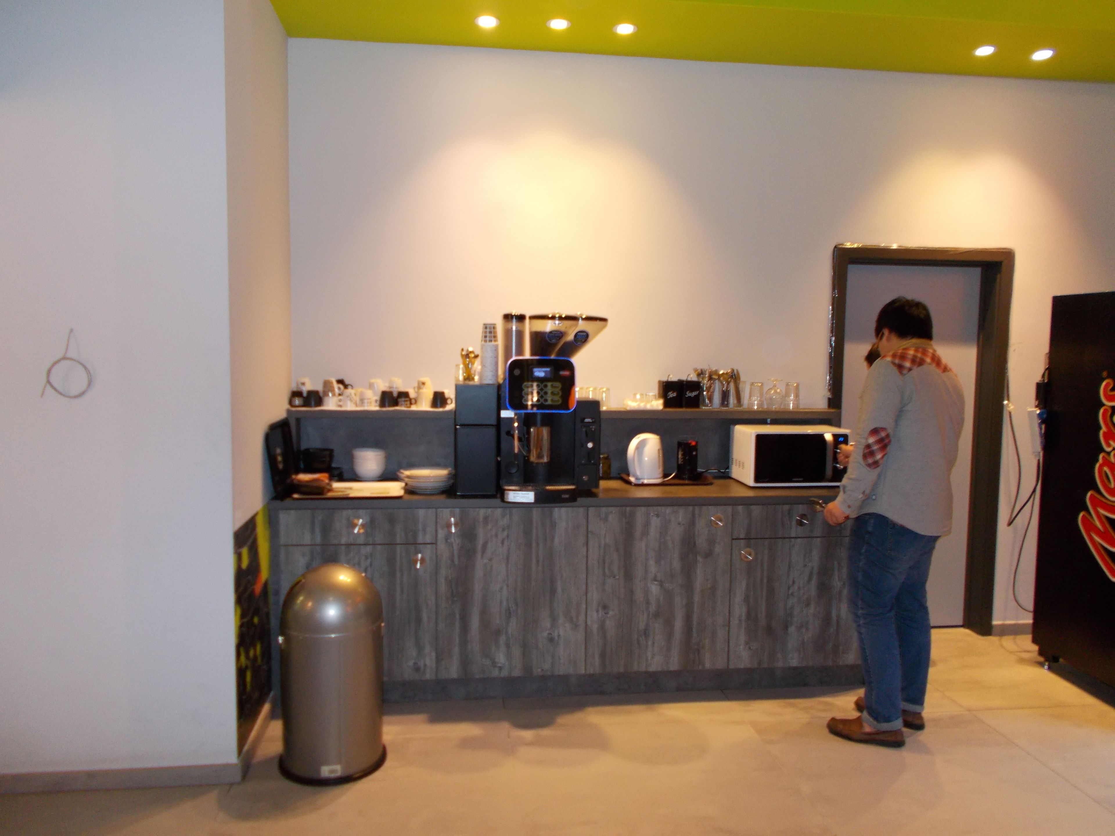 A modern kitchen with a coffee machine, microwave, and a person standing near the counter.