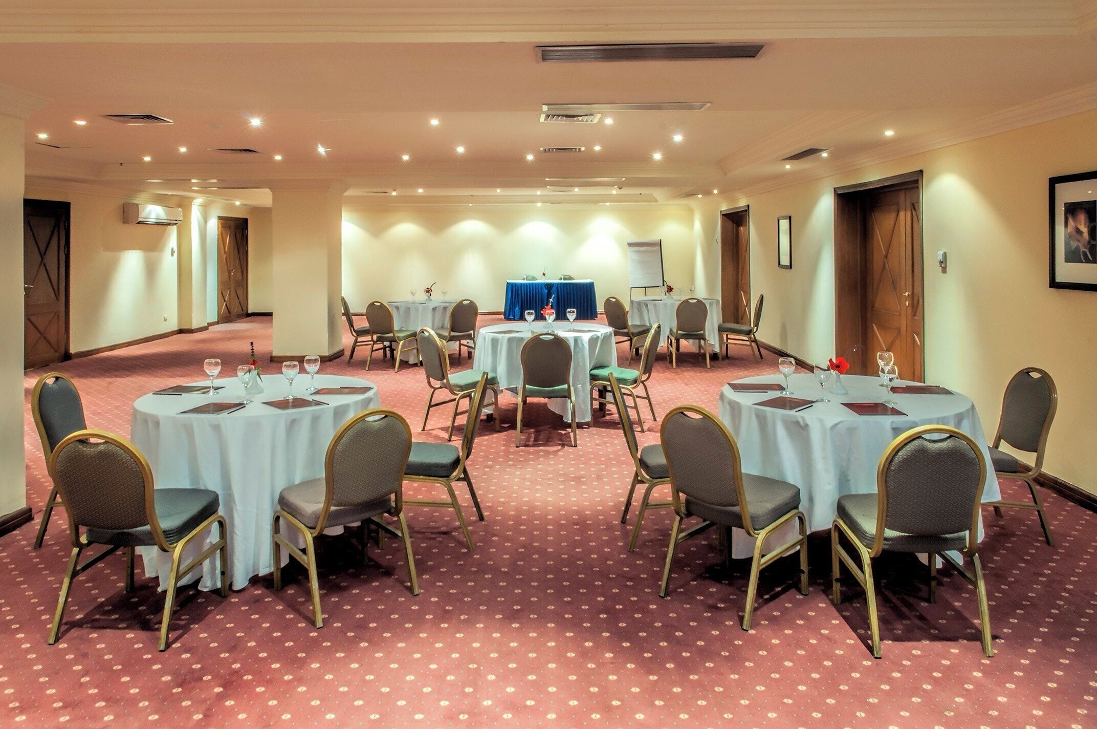 A conference room with multiple round tables, each with chairs, and a blue tablecloth at the center.