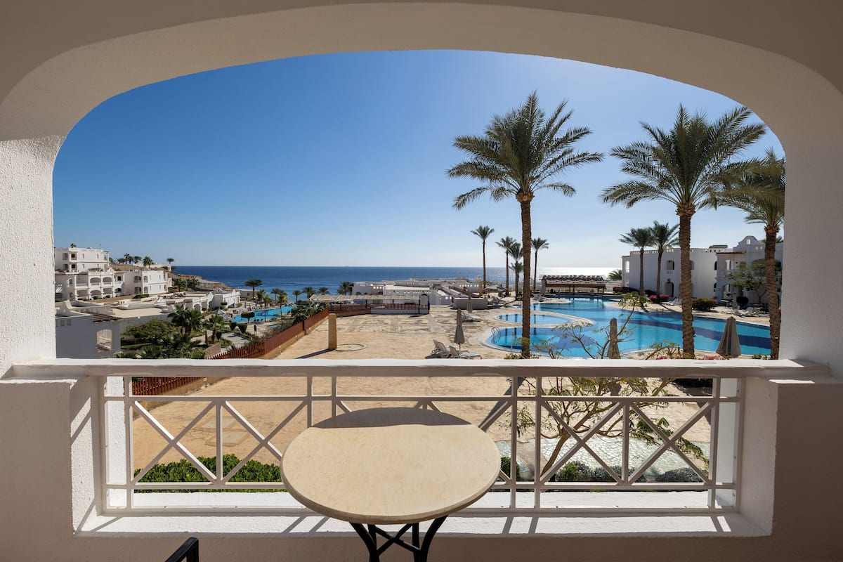 Un balcón con vista a una playa, una piscina y palmeras.
