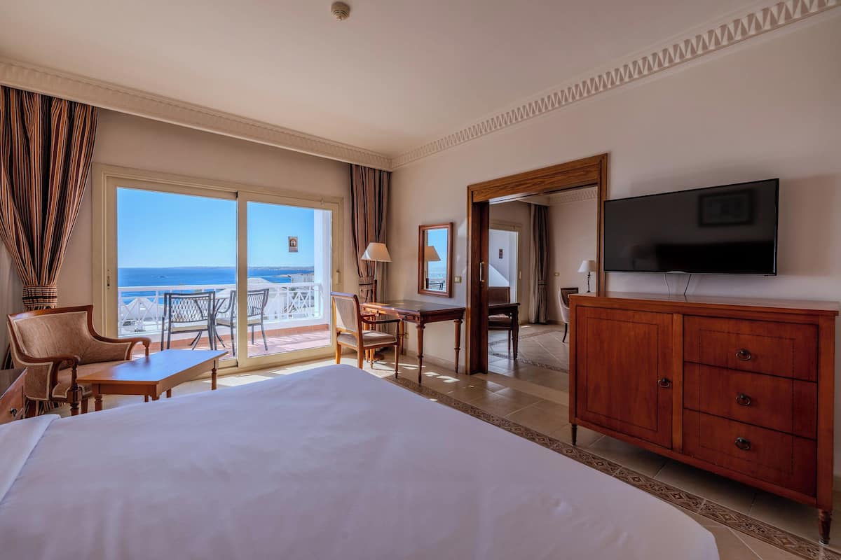 Habitación de hotel con una cama grande, un escritorio, una silla, un televisor y un balcón con vista al mar.