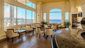A spacious lobby with a curved marble reception desk, multiple seating areas with chairs and tables, large windows with decorative glass, and a view of the ocean. - Continental Plaza Beach Resort (Sharm El Sheikh)