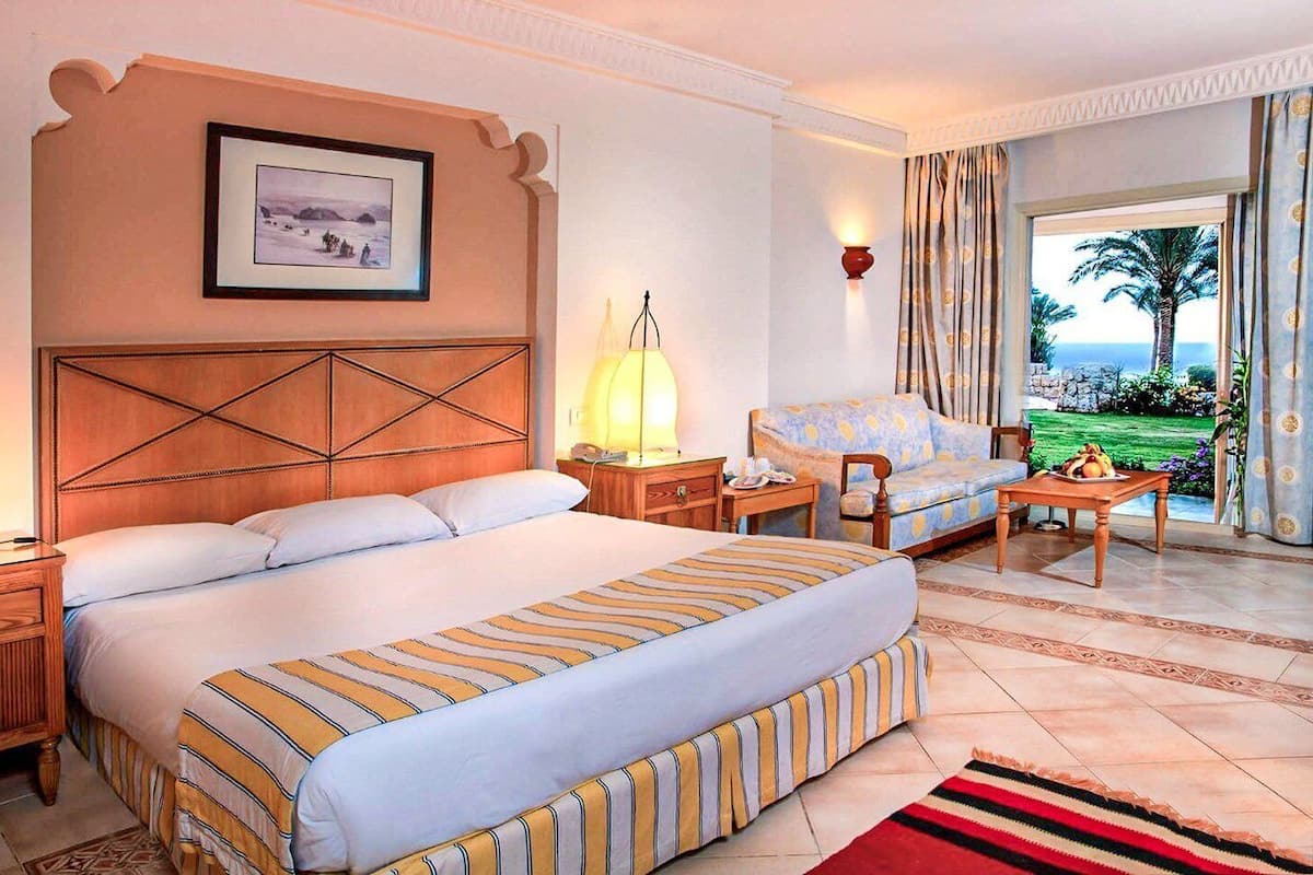 Habitación de hotel con una cama grande, un sofá, un escritorio, una lámpara y vistas al océano.
