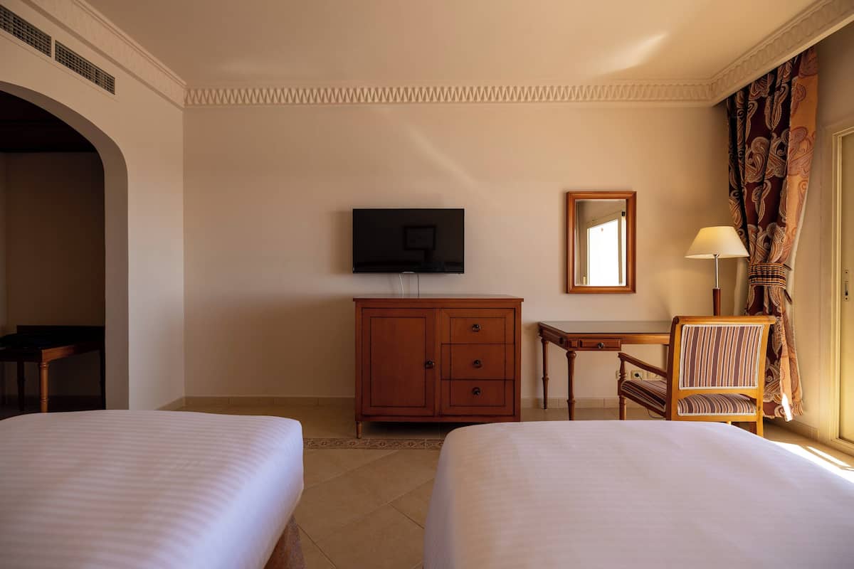 Habitación de hotel con dos camas, televisión, armario de madera, escritorio, silla y espejo.